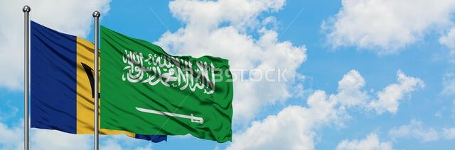 يرفرف علما بربادوس والمملكة العربية السعودية معاً في مهب الريح أمام سماء زرقاء صافية تتخللها غيوم بيضاء. مفهوم الدبلوماسية، العلاقات الدولية.