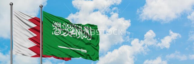 يرفرف علم البحرين والسعودية معاً في مهب الريح أمام سماء زرقاء صافية تتخللها غيوم بيضاء. مفهوم الدبلوماسية، العلاقات الدولية.