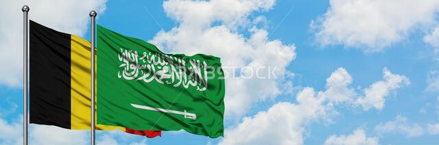 يرفرف علم بلجيكا والسعودية معاً في مهب الريح أمام سماء زرقاء صافية تتلألأ بالغيوم البيضاء. مفهوم الدبلوماسية، العلاقات الدولية.