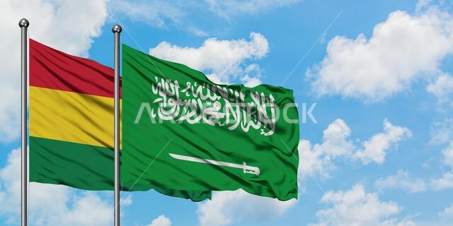 يرفرف علم بوليفيا وعلم المملكة العربية السعودية معاً في مهب الريح أمام سماء زرقاء ملبدة بالغيوم البيضاء. مفهوم الدبلوماسية، العلاقات الدولية.