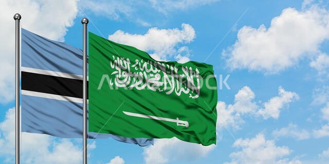 يرفرف علم بوتسوانا وعلم المملكة العربية السعودية معاً في مهب الريح أمام سماء زرقاء صافية تتلألأ فيها الغيوم البيضاء. مفهوم الدبلوماسية، العلاقات الدولية.