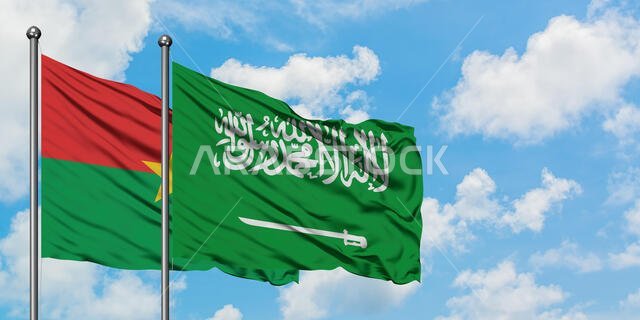 يرفرف علم بوركينا فاسو وعلم المملكة العربية السعودية معاً في مهب الريح أمام سماء زرقاء صافية تتخللها غيوم بيضاء. مفهوم الدبلوماسية، العلاقات الدولية.