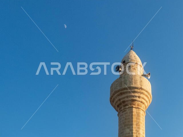 مئذنة المسجد مقابل السماء الزرقاء والقمر عند الغروب. مئذنة المسجد مقابل السماء الزرقاء والقمر عند الغروب.