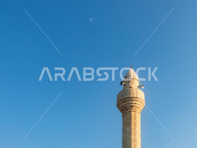 Mosque minaret opposite evening blue sky and moon.