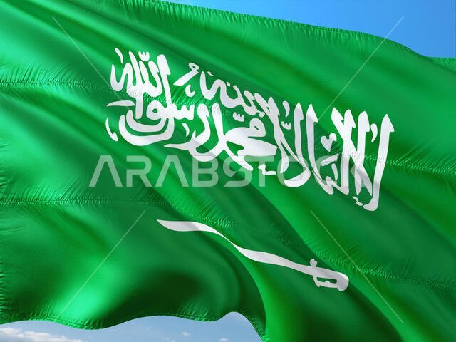 علم المملكة العربية السعودية يرفرف في مهب الريح على خلفية سماء زرقاء صافية. قماش عالي الجودة.
