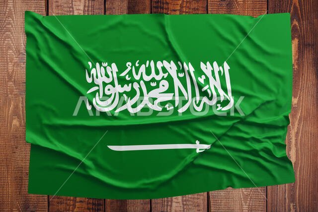 علم المملكة العربية السعودية على خلفية طاولة خشبية. علم سعودي مجعد من الأعلى.
