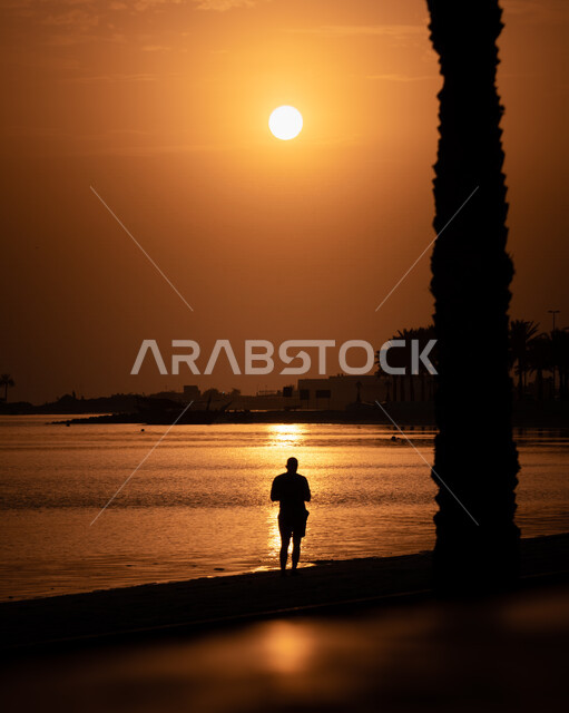 صورة ظلية لرجل عربي خليجي سعودي يقف على شاطيء البحر اثناء غروب الشمس، اماكن ساحلية، جمال الطبيعة في المملكة العربية السعودية، السياحة في السعودية