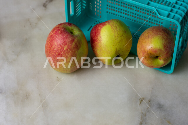 صورة مقربة لفاكهة التفاح بجانب صندوق بلاستيكي على خلفية من الرخام الأبيض ، الفواكه الطازجة ، فطور صحي ، حمية غذائية مفيدة ، فاكهة التفاح اللذيذة والصحية ، فاكهة صيفية 