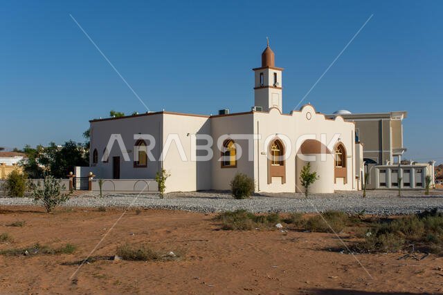 المسجد الأبيض في منطقة سكنية في الشرق الأوسط، تحت سماء زرقاء في ضوء شمس العصر المتأخر.