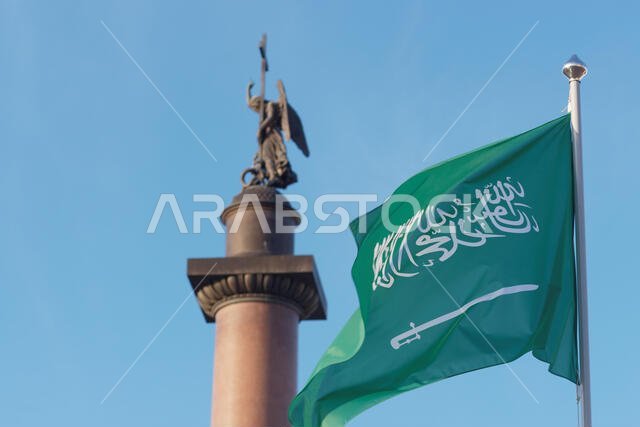 Flag of the Kingdom of Saudi Arabia waving against the statue of angel on the top of Alexander Column in Saint-Petersburg, Russia