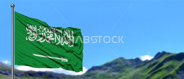 علم المملكة العربية السعودية يرفرف في السماء الزرقاء مع حقول خضراء على قمة جبل في الخلفية. موضوع طبيعي.