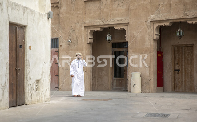 رجل عربي خليجي عماني يتجول في شوارع حي السيف بدبي في الإمارات العربية المتحدة، احياء المدينة القديمة بدبي، التجول في احياء دبي، البيوت الشعبية التاريخية القديمة، معالم دبي المشهورة، صورة الجسم بالطول الكامل، السياحة في الامارات