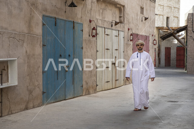 رجل عربي خليجي عماني يتجول في شوارع حي السيف بدبي في الإمارات العربية المتحدة، احياء المدينة القديمة بدبي، التجول في احياء دبي، البيوت الشعبية التاريخية القديمة، معالم دبي المشهورة، صورة الجسم بالطول الكامل، السياحة في الامارات