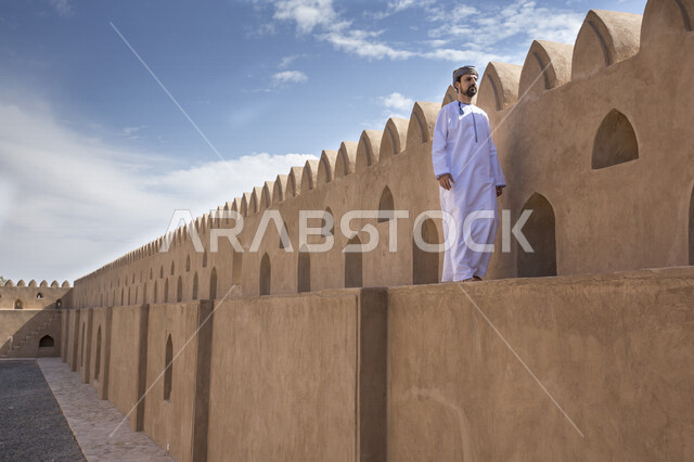 رجل عربي خليجي عماني يتجول فوق جدار احد القلاع في حي السيف بدبي في الإمارات العربية المتحدة، احياء المدينة القديمة بدبي، التجول في احياء دبي، البيوت الشعبية القديمة، معالم دبي المشهورة، صورة الجسم بالطول الكامل، السياحة في الإمارات