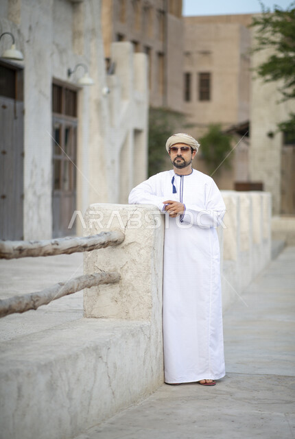 رجل عربي خليجي عماني يرتدي النظارات الشمسية ويقف في شوارع حي السيف بدبي في الإمارات العربية المتحدة، الوقوف بثقة، البيوت الشعبية القديمة، المدينة القديمة بدبي، حي السيف، معالم دبي المشهورة، صورة الجسم بالطول الكامل، السياحة في الإمارات