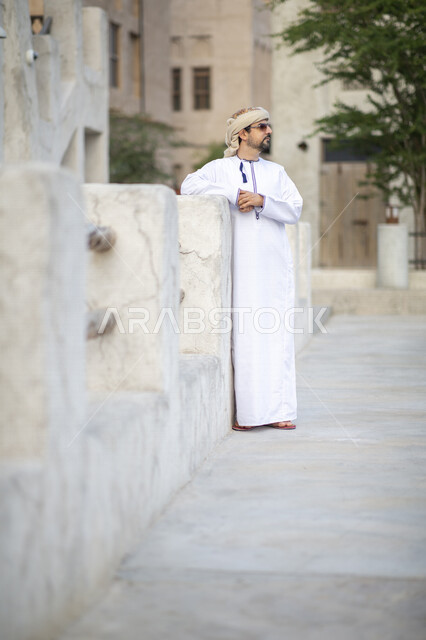 رجل عربي خليجي عماني يرتدي النظارات الشمسية ويقف في شوارع حي السيف بدبي في الإمارات العربية المتحدة، الوقوف بثقة، البيوت الشعبية القديمة، المدينة القديمة بدبي، حي السيف، معالم دبي المشهورة، صورة الجسم بالطول الكامل، السياحة في الإمارات