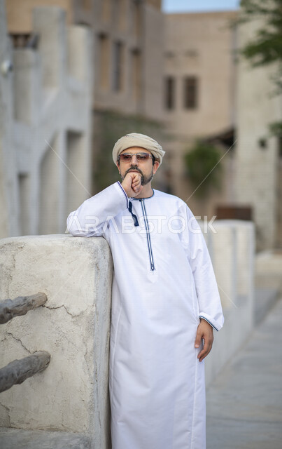 رجل عربي خليجي عماني يرتدي النظارات الشمسية ويقف في شوارع حي السيف بدبي في الإمارات العربية المتحدة، الوقوف بثقة، البيوت الشعبية القديمة، المدينة القديمة بدبي، حي السيف، معالم دبي المشهورة، صورة الجسم بالطول الكامل، السياحة في الإمارات