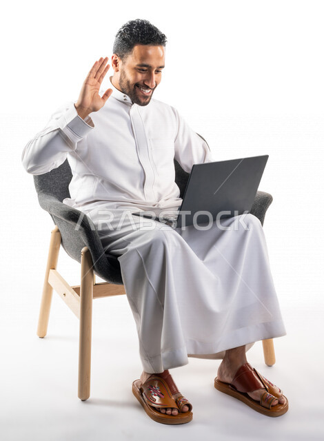 بورتريه لرجل عربي خليجي سعودي يجلس على كرسي يحمل بيده جهاز الحاسوب، اجراء مكالمات فيديو، تواصل اجتماعي، محادثات ودردشة، التواصل مع الأصدقاء، اجتماع عمل عن بعد، بث فيديو مباشر، خلفية بيضاء