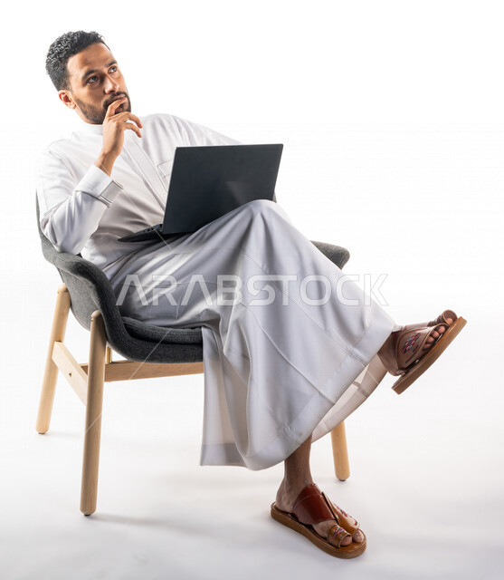 بورتريه لرجل عربي خليجي سعودي يجلس على كرسي يحمل بيده جهاز الحاسوب، اجراء مكالمات فيديو، تواصل اجتماعي، محادثات ودردشة، التواصل مع الأصدقاء، اجتماع عمل عن بعد، بث فيديو مباشر، خلفية بيضاء