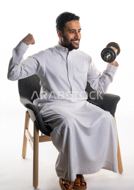 بورتريه لرجل عربي خليجي سعودي يجلس على كرسي يقوم بممارسة التمارين الرياضية بالدمبل ، نشاط بدني للمحافظة على الصحة و اللياقة الجسدية ، تقوية عضلات الجسم و بنائها ، تمارين رفع الأثقال (دمبلز)، رفع الأوزان الحديدية الثقيلة ، كمال الأجسام ، لياقة و رشاقة