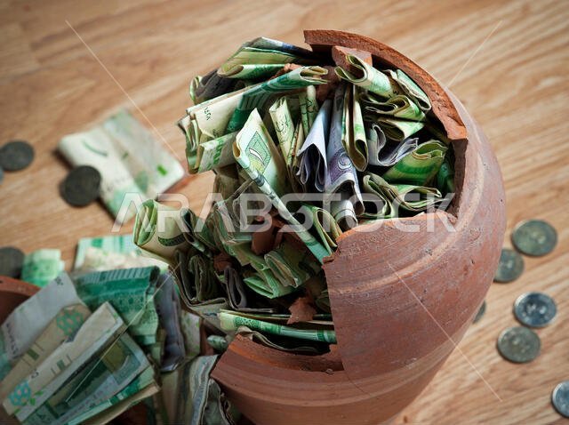 حصالة نقود مكسورة، تحتوي على أوراق نقدية وعملات معدنية من الريال السعودي