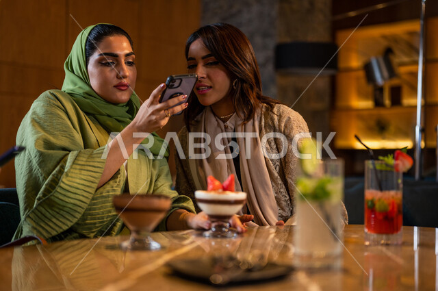 صديقات عربيات خليجيات سعوديات يجلسن في المقهى، توثيق اللحظات الجميلة بإستخدام الهاتف المحمول، علاقات إجتماعية بين الإصدقاء، إستخدام وسائل التواصل الإجتماعي، قضاء أوقات ممتعة مع الأصدقاء، جلسة وناسة وتعارف، فن وموهبة تصوير المأكولات والمشروبات