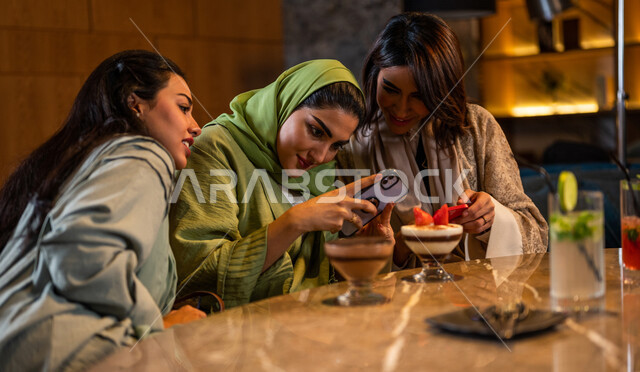 صديقات عربيات خليجيات سعوديات يجلسن في المقهى، توثيق اللحظات الجميلة بإستخدام الهاتف المحمول، علاقات إجتماعية بين الإصدقاء، إستخدام وسائل التواصل الإجتماعي، قضاء أوقات ممتعة مع الأصدقاء، جلسة وناسة وتعارف، فن وموهبة تصوير المأكولات والمشروبات