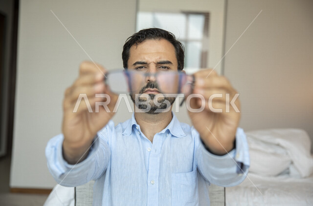 رجل عربي يحمل بيده النظارة الطبية خاصة بضعف النظر ، الرؤية من خلال النظارة الطبية ، مفهوم ضعف البصر ، قصر النظر