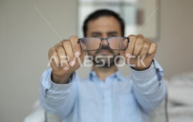 رجل عربي يحمل بيده النظارة الطبية خاصة بضعف النظر ، الرؤية من خلال النظارة الطبية ، مفهوم ضعف البصر ، قصر النظر