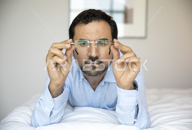 رجل عربي مستلقي على بطنه ، يرتدي النظارات الطبية خاصة بضعف النظر، النظر إلى الكاميرا ، الشعور بالضجر والملل ، الرؤية بالنظارات الطبية ، روتين ممل ، ضعف البصر