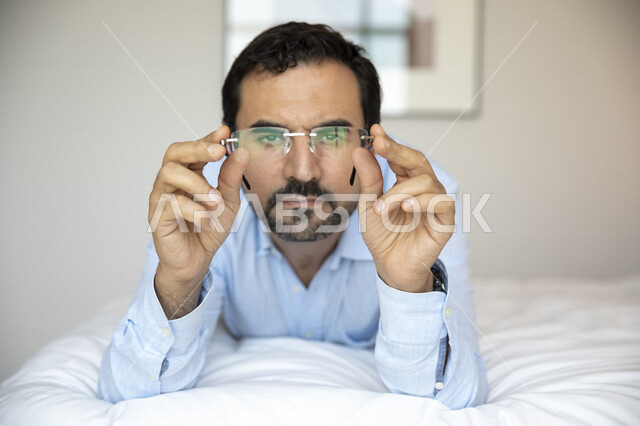 رجل عربي مستلقي على بطنه ، يرتدي النظارات الطبية خاصة بضعف النظر، النظر إلى الكاميرا ، الشعور بالضجر والملل ، الرؤية بالنظارات الطبية ، روتين ممل ، ضعف البصر