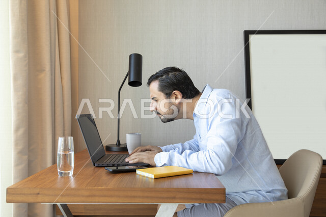 رجل عربي يقوم بإستخدام جهاز الحاسوب المحمول، العمل عن بعد ، تصفح الإنترنت ،  جلسة عمل ، ضعف الرؤية ، صعب القراءة ، مشاكل النظر ، قصر النظر