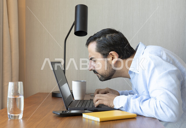 رجل عربي يقوم بإستخدام جهاز الحاسوب المحمول، العمل عن بعد ، تصفح الإنترنت ،  جلسة عمل ، ضعف الرؤية ، صعب القراءة ، مشاكل النظر ، قصر النظر
