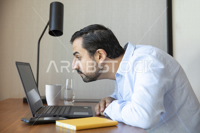 رجل عربي يقوم بإستخدام جهاز الحاسوب المحمول، العمل عن بعد ، تصفح الإنترنت ،  جلسة عمل ، ضعف الرؤية ، صعب القراءة ، مشاكل النظر ، قصر النظر