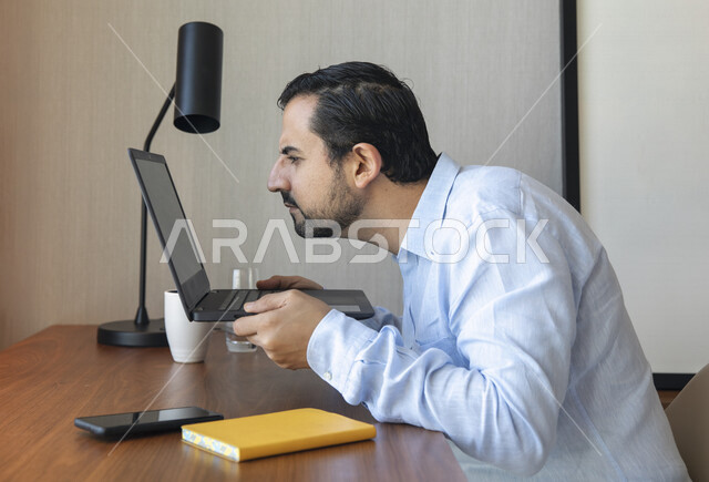 رجل عربي يقوم بإستخدام جهاز الحاسوب المحمول، العمل عن بعد ، تصفح الإنترنت ،  جلسة عمل ، ضعف الرؤية ، صعب القراءة ، مشاكل النظر ، قصر النظر