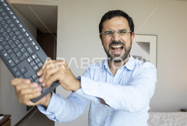 رجل عربي يرتدي النظارات الطبية لضعف النظر، يحمل بيده لوحة المفاتيح بإيماءات تدل على الغصب والتعصب ، مفهوم التوتر و الضغط العصبي والنفسي ، الشعور بالضجر  و الإنزعاج