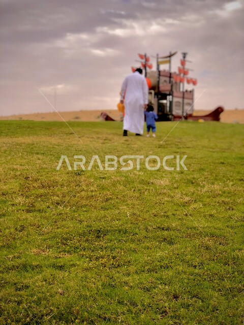 صورة من الخلف لرجل عربي خليجي سعودي يمسك بطفلته، حدائق السعودية، مناظر طبيعية خلابة، نزهة عائلية، الطبيعة في السعودية، اماكن سياحية