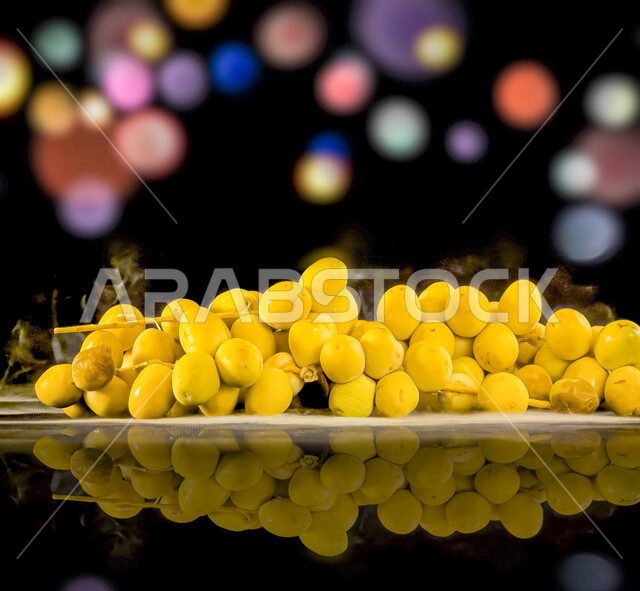Close-up of yellow plate of dates, reflection of plate of dates on glass, healthy meal, delicious bunch of dates, black background