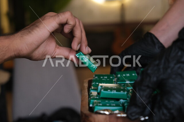 صورة مقربة ليد رجل عربي خليجي سعودي يمسك حبة الشوكلاتة، قطع الشوكلاتة، شوكلاتة اليوم الوطني السعودي، الاحتفال بيوم الاستقلال السعودي، اليوم الوطني السعودي