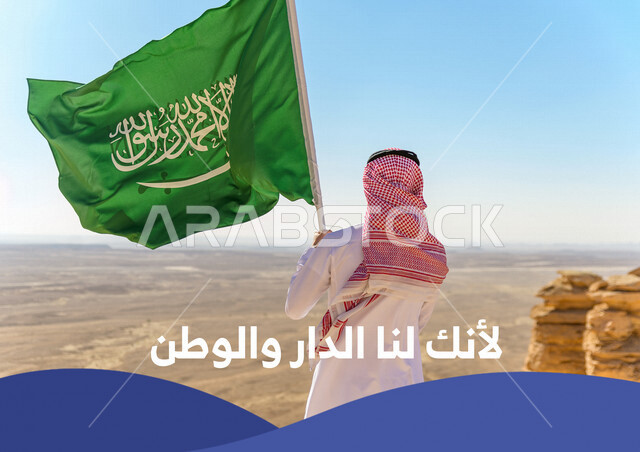 صورة مقربة بزاوية من الخلف لرجل عربي خليجي سعودي يحمل علم المملكة العربية السعودية في المناطق الصحراوية، هوية اليوم الوطني السعودي 92 ، شعار لأنك لنا الدار والوطن، تصميم غلاف ( كفر ) ، حب الوطن