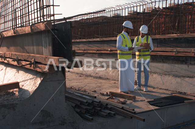 مهندسان معماريان سعوديان خليجيان يناقشان مخطط لمشروع البناء، إرتداء سترة الحماية الخاصة بالعمل، تدقيق العمل، الإشراف والنقاش لمشاريع قيد الانشاء، مفهوم الهندسة المعمارية، إدارة المشاريع الهندسية، مهن ووظائف هندسية، مخططات وتصماميم هندسية