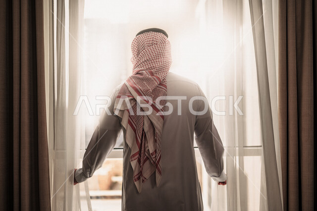 رجل عربي خليجي سعودي يقف امام النافذة، غرفة فندقية، النظر الى الخارج من خلال النافذة، إشراقة يوم جديد، مفهوم الهمة والنشاط، التخخطيط المستقبلي، الرؤية المستقبلية، سياحة وفندقة
