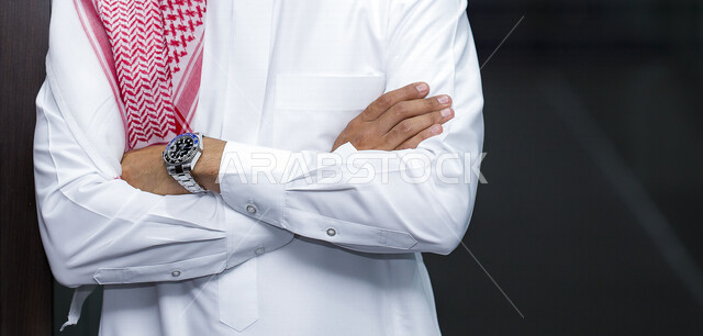بورتريه لرجل عربي سعودي خليجي يرتدي الثوب السعودي، منظر أمامي لرجل سعودي بأيدي متقاطعه, تصوير من الأمام لرجل سعودي يقف متكتف اليدين, الوقوف بثقه, خلفيه سوداء