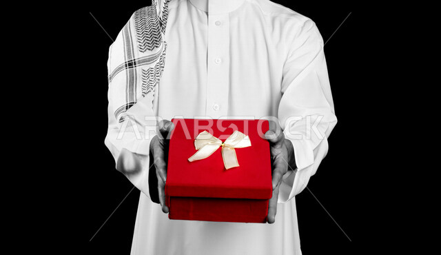 بورتريه لرجل عربي سعودي خليجي يحمل بيده علبة حمراء، إيماءات يدين تدل على الحب والفرح والسعادة, هدايا ومناسبات, أعياد ميلاد, مناسبات عائليه, مفاجآت وهدايا العيد, خلفية سوداء