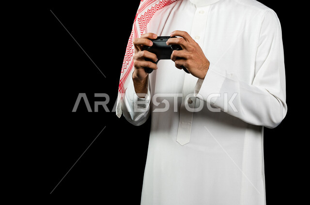 بورتريه لرجل عربي سعودي خليجي يمسك بيده عصا التحكم و يلعب بألعاب الفيديو، المتعة و التسلية بألعاب الفيديو، ألعاب البلايستيشن الترفيهية، تقنيات و ألعاب, قضاء وقت ممتع, خلفيه سوداء