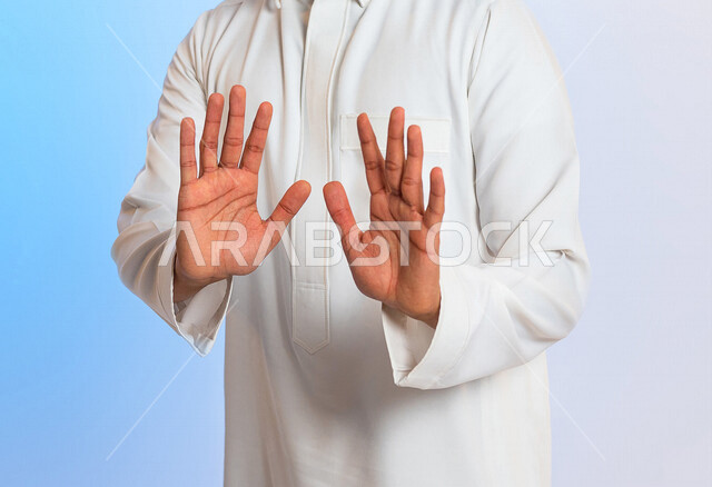 بورتريه لرجل عربي سعودي خليجي يرتدي الثوب السعودي, إيماءات يدين تدل على الأمر بالتوقف عن فعل شيء ما, الشعور بالخوف و الإنزعاج, الرفض والإمتناع , خلفية ملونه