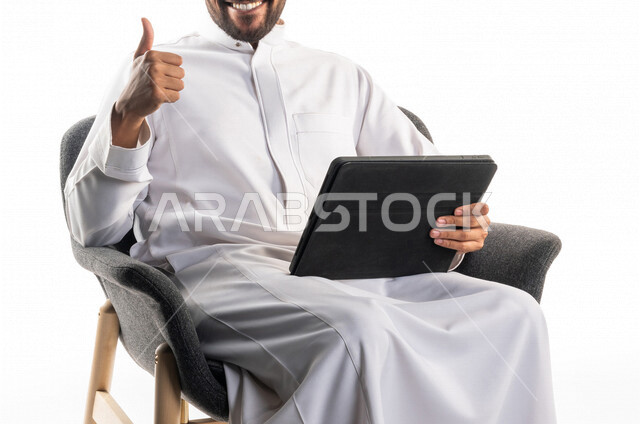 بورتريه لرجل عربي خليجي سعودي يجلس على كرسي يحمل بيده جهاز الحاسوب يرفع اصبع الإبهام، الجوده والإمتياز, تقييم الخدمه، تواصل اجتماعي، محادثات ودردشة، التواصل مع الأصدقاء، اجتماع عمل عن بعد، بث فيديو مباشر، خلفية بيضاء