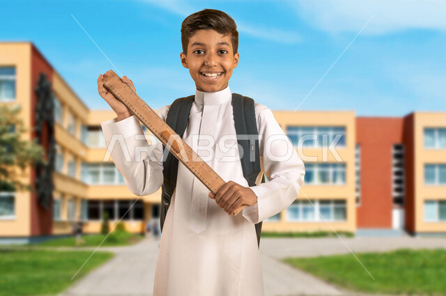 طالب عربي خليجي سعودي يمسك مسطرة مرقمة ويرتدي الزي المدرسي، حقيبة الظهر المدرسية، أدوات قرطاسية، الإستعداد للعام الدراسي الجديد، التعليم في السعودية، العودة إلى المدارس