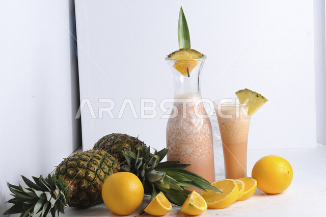 كوب من عصير الفواكه المشكل اللذيذ، مشروب بارد من الفواكه، مشروبات باردة، عصائر طبيعية لذيذة، عصير صحي ومفيد، كوكتيل صيفي منعش ومثلج، كوب زجاجي، حبات من فاكهة الاناناس والبرتقال، خلفية بيضاء