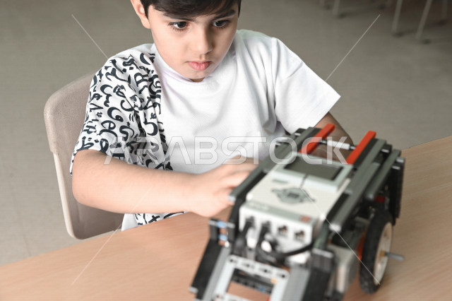 طفل عربي سعودي خليجي يقوم بتركيب وتطوير سيارة روبوت , تركيب الأجزاء والقطع لصناعة سيارة تعمل آليا , تعلم الإبتكار وزيادة ذكاء الطفل عن طريق صناعة الأعمال اليدوية .